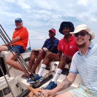 Combo Course- Yacht crew & Day Skipper: This image is showing a group of friends with beaming smiles enjoys a sunny day sailing off the coast of Durban, South Africa. The sparkling ocean and clear blue sky provide a picturesque backdrop as they share laughter