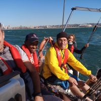 Coastal Skipper: An image capturing the transformation of a novice sailor into a skilled coastal skipper. The student confidently handles the helm of a yacht, navigating through coastal waters with ease and precision. In the background, the Durban skyline appears on the horizon on a sunny day.