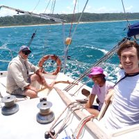 Combo Course- Yacht crew & day Skipper: This image shows a group of Offshore Sailing Academy students with big smiles enjoying a day on the Indian Ocean. In the background, The sparkling ocean, clear blue sky and the South African coast line appearing on the horizon on a sunny day.