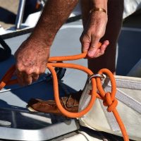 Sailing Academy Durban -This image is showing a close-up image of students diligently practicing knots and rigging techniques on the deck of a yacht. Their hands expertly maneuvering ropes under the guidance of an instructor, preparing them for yacht crew roles.